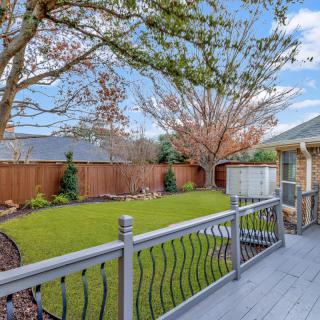 A peaceful backyard with a wooden deck overlooking a green lawn and trees.