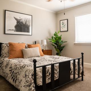 A cozy bedroom with a neatly made bed, featuring decorative pillows and floral bedding, complemented by wall art and a lush potted plant.