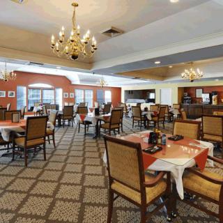 An elegant dining room with neatly arranged tables and chairs, featuring chandeliers and a patterned carpet.