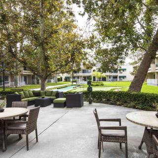 A tranquil outdoor patio with tables and chairs surrounded by lush greenery and trees.