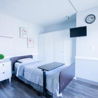 A clean and organized hospital room featuring a single bed, bedside table, television, and simple decor.