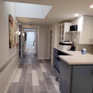 A modern interior hallway with a kitchenette, featuring white cabinets and wood flooring.