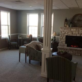 A cozy living room with multiple chairs and a fireplace, bathed in natural light from large windows.