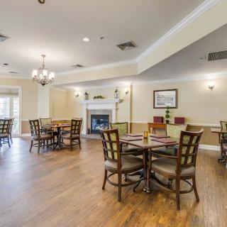 A spacious dining area with multiple tables, chairs, and a fireplace, featuring a wooden floor and bright lighting.