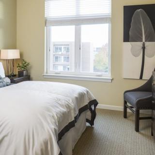 A cozy bedroom with a neatly made bed, a window letting in natural light, and minimalist decor.