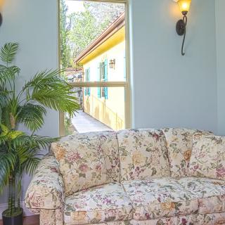 A cozy living room with a floral sofa, decorated with wall sconces and an indoor plant, offering a view through the window.