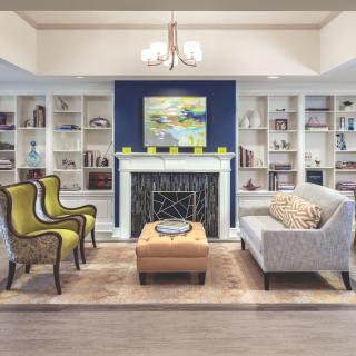A stylish living room featuring a cozy fireplace, elegant armchairs, and a modern sofa amidst well-organized bookshelves.
