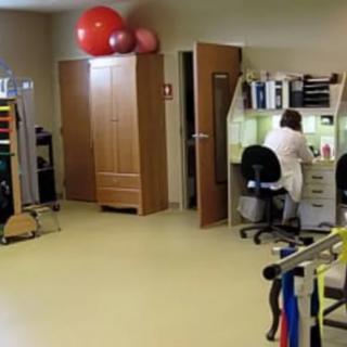 A rehabilitation clinic with exercise equipment and a healthcare professional working at a desk.