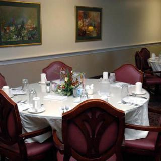 A formal dining room setup with a round table, white tablecloth, and elegant chairs, surrounded by artwork on the walls.