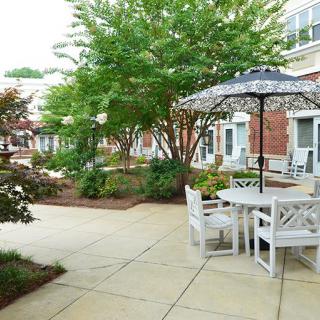 A peaceful courtyard featuring outdoor seating with tables and umbrellas surrounded by lush greenery.