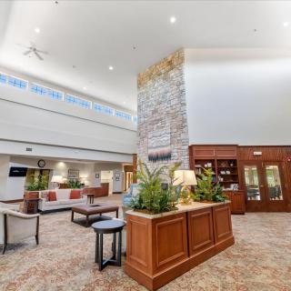 A spacious hotel lobby featuring a stone fireplace, seating area, and indoor plants.
