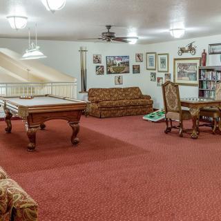 A cozy game room featuring a billiards table, sofas, and various artworks adorning the walls.