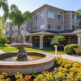 A modern building with a beautiful garden and fountain under a sunny sky.