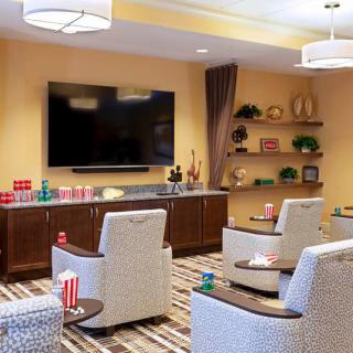 A modern and cozy living room with comfortable chairs facing a large television, complemented by decorative shelves in the background.