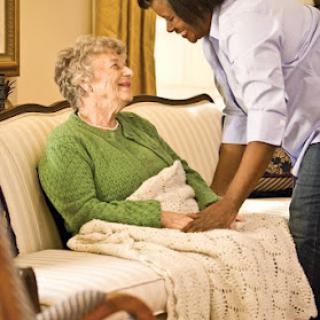 A caregiver providing comfort and companionship to an elderly woman on a sofa.