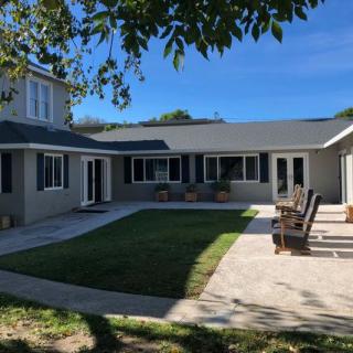 A spacious backyard with a lawn, patio seating, and a modern house under a clear blue sky.