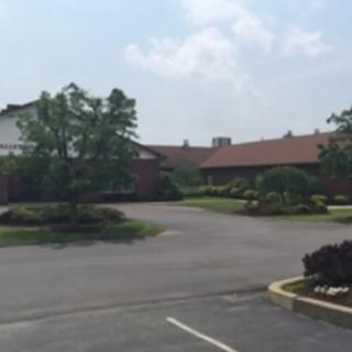 A view of a parking lot in front of a building surrounded by trees under a partly cloudy sky.