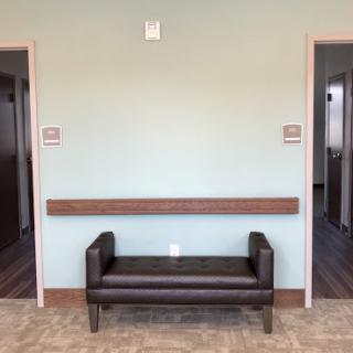 A waiting area featuring a simple bench between two doorways, with a soothing wall color.