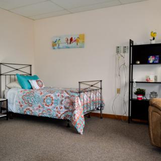 A cozy bedroom with a single bed, decorative pillows, wall art, and shelving unit.