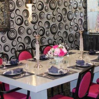 A stylish dining room features a modern table setting with pink chairs and a bold, circular-patterned wallpaper.