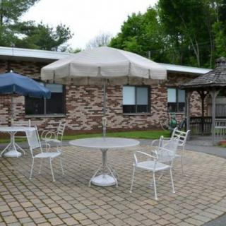 An outdoor patio setup with tables, chairs, and umbrellas against a brick wall backdrop.