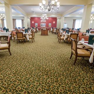 A spacious dining area with neatly arranged tables and chairs, featuring elegant chandeliers and a patterned carpet.