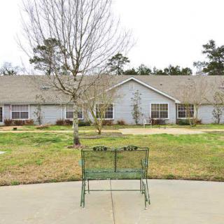 A view of a single-story building with a bench in the foreground and trees in the yard.
