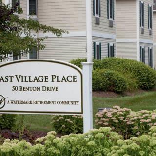 Sign for East Village Place, a retirement community, with landscaped gardens and building in the background.