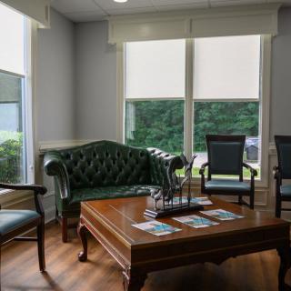 A cozy waiting area with a green sofa, chairs, and a wooden coffee table by large windows.