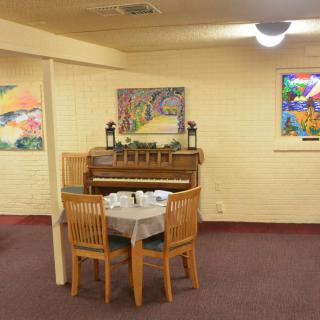A cozy room with a piano and a small dining table surrounded by chairs, adorned with colorful wall paintings.