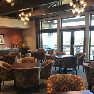 A cozy restaurant interior with tables and chairs arranged under decorative chandeliers, featuring large windows.