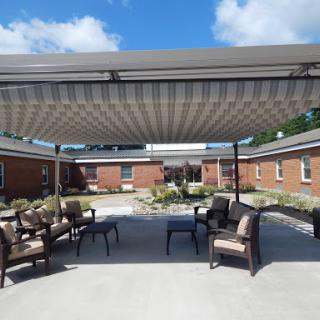A cozy outdoor seating area with a sunshade, surrounded by greenery and buildings under a partly cloudy sky.