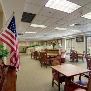 A spacious meeting room with tables and chairs, featuring an American flag and natural lighting from large windows.