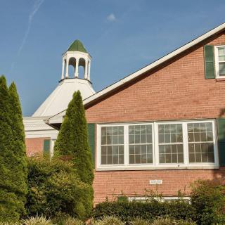 A brick building with a dome and green shutters surrounded by trees and greenery.