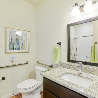 A clean and modern bathroom with granite countertops and a well-lit mirror.