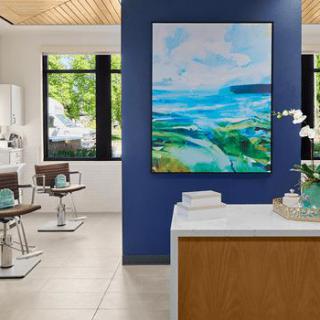 A modern salon interior featuring stylish chairs, a reception desk, and a vibrant piece of artwork on the wall.