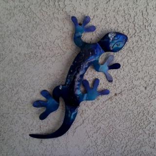 Blue decorative metal lizard hanging on a wall.
