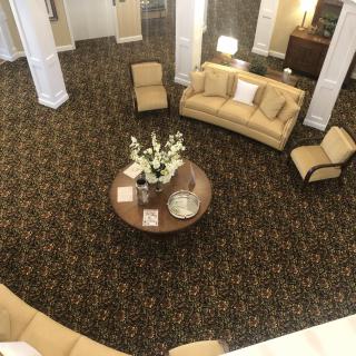 A spacious, elegantly decorated lobby with sofas, chairs, a round table, and decorative elements on the carpeted floor.