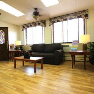 A cozy living room with a black sofa, wooden coffee tables, and a ceiling fan.