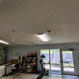 A well-lit office workspace featuring a desk, shelves, and various equipment.