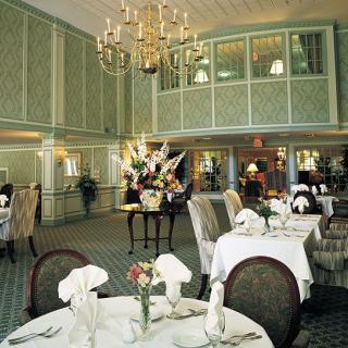 A luxurious restaurant interior featuring elegant dining tables, a grand chandelier, and floral decorations.