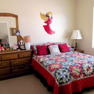 A cozy bedroom with a colorful quilt, decorated with an angel figure above the bed.