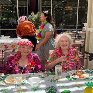 A joyful gathering of seniors enjoying a festive celebration with colorful leis and delicious food.