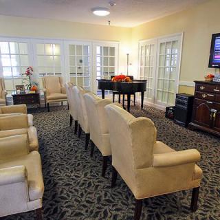 A cozy living room with upholstered chairs, a piano, and a television.