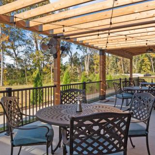 An inviting outdoor patio area with wrought iron furniture under a wooden pergola, surrounded by lush greenery.