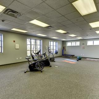 An empty gym room featuring stationary bikes and yoga mats, with large windows providing natural light.