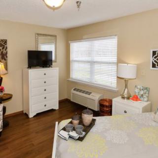 A cozy bedroom with a white dresser, television, and a well-lit window.