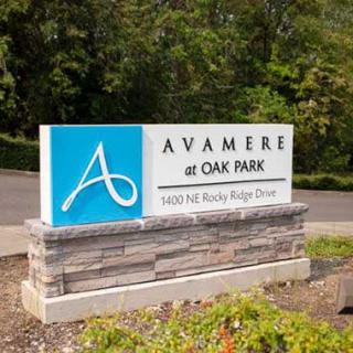 Sign for Avamere at Oak Park near a driveway surrounded by greenery.