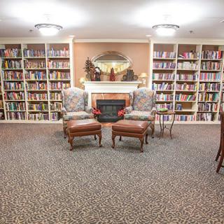 A cozy library with bookshelves, comfortable chairs, and a fireplace.