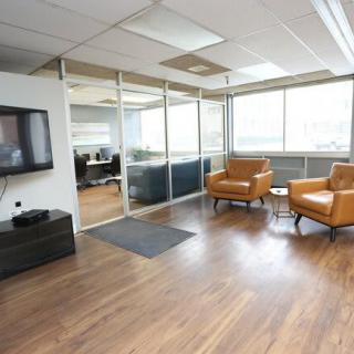 A modern office lobby with two brown chairs, a television, and a glass partition.